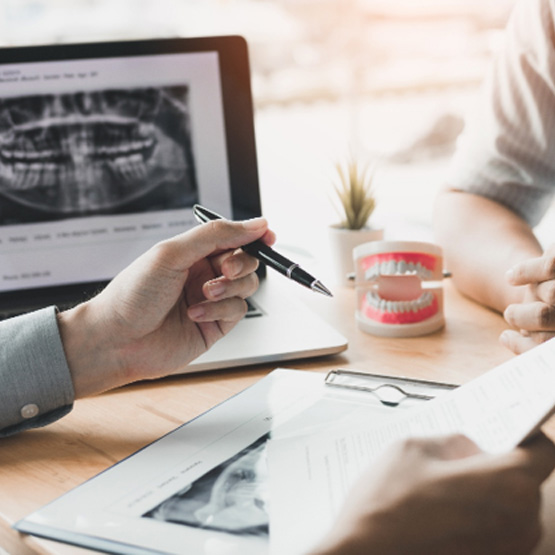 Hands of dentist and patient at desk with papers, X-rays, and model teeth