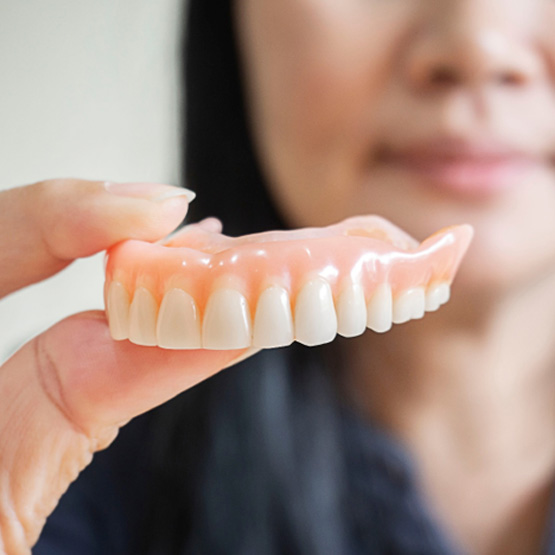 Woman holding upper arch of dentures to the camera