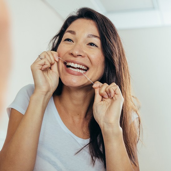 Woman smiling while flossing in bathroom