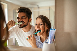 Couple smiling while brushing teeth in bathroom