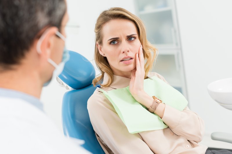 Patient holding cheek at dentist due to toothache